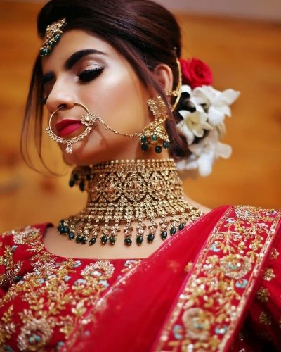 Photo of Bride twirling in red and gold lehenga with green jewellery